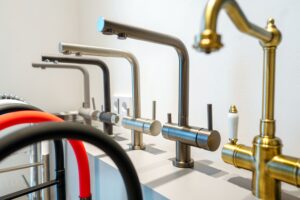A variety of modern kitchen faucets on display in a showroom, featuring stainless steel, brass, and colored designs.