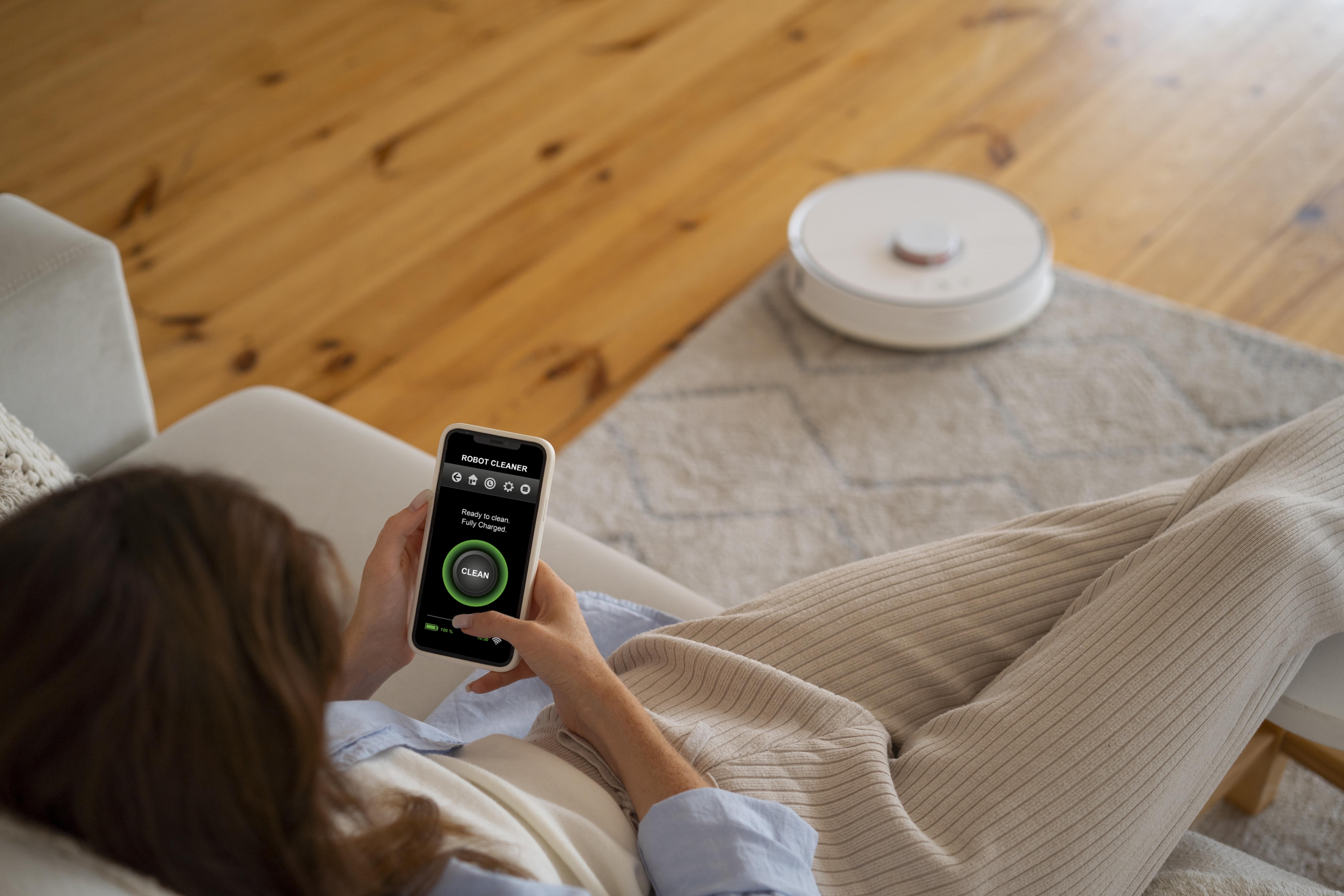 Person controlling robot vacuum cleaner with smartphone app